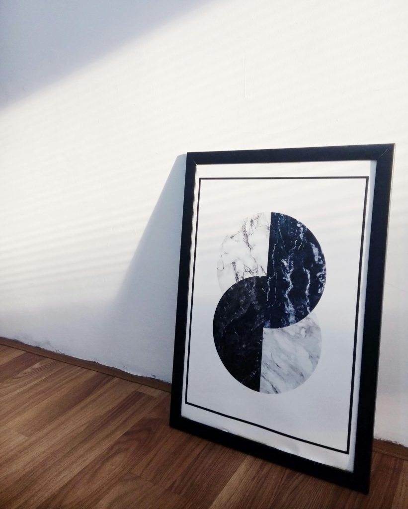A framed minimalist abstract artwork in a sunlit room on wooden floor.